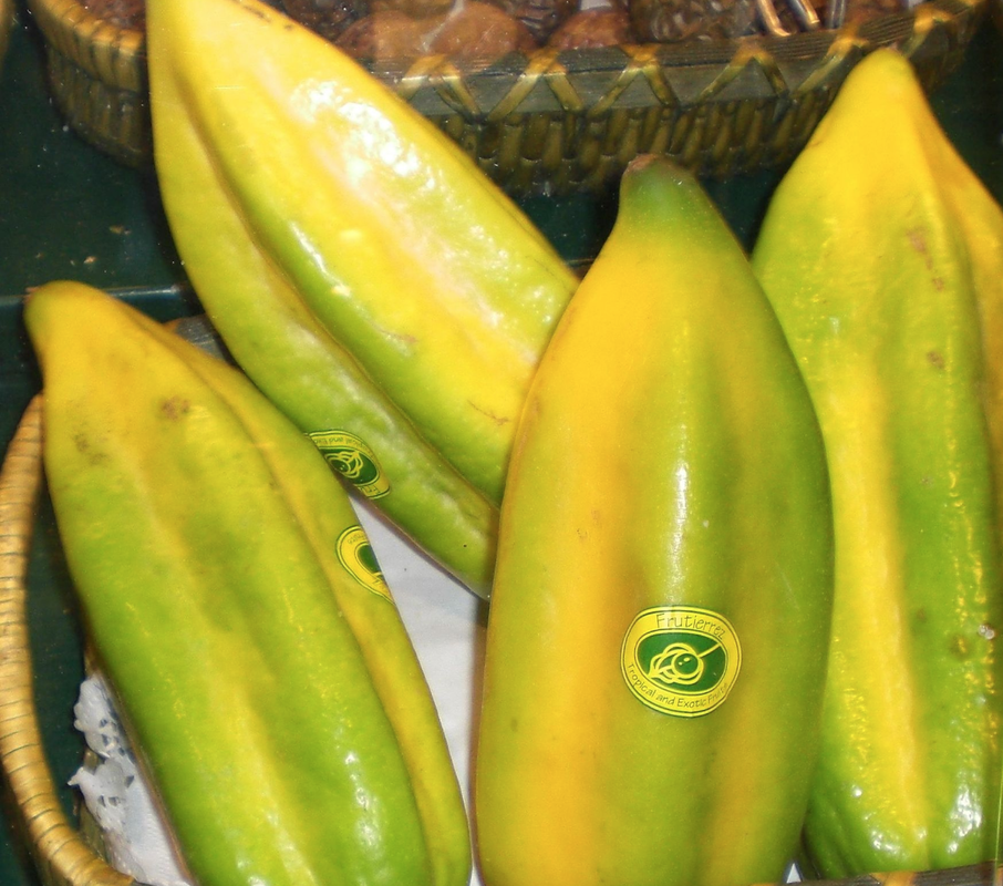 Four ripe 5-sided babaco fruits showing green to yellow skin. Three fruits exhibit oval produce stickers.