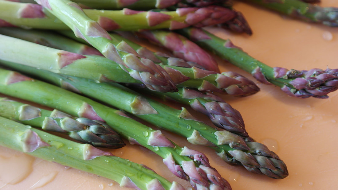 Several fresh stalks of green asparagus with purple tips on orange-tan surface